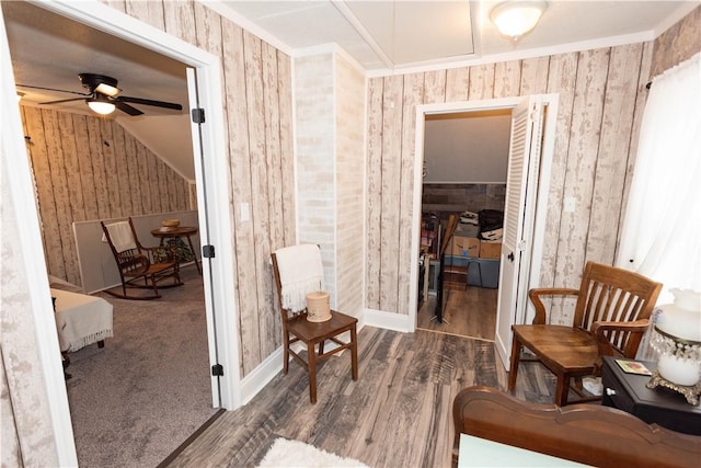 sitting room with wallpapered walls, a ceiling fan, wood finished floors, ornamental molding, and baseboards