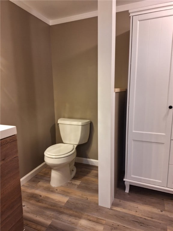 bathroom with toilet, wood finished floors, baseboards, vanity, and ornamental molding