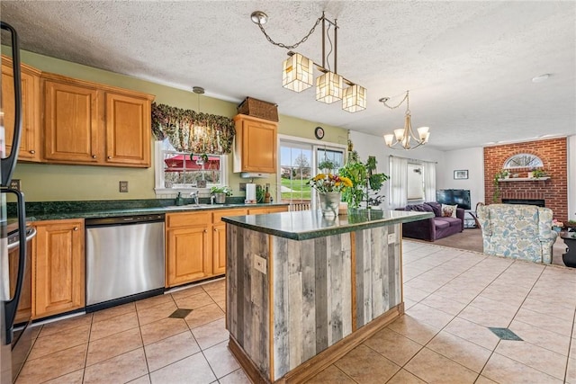kitchen with a notable chandelier, light tile patterned floors, dark countertops, a brick fireplace, and dishwasher
