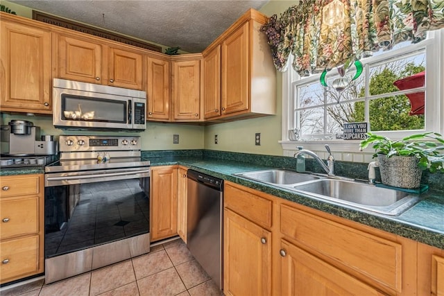 kitchen with light tile patterned floors, a textured ceiling, dark countertops, appliances with stainless steel finishes, and a sink