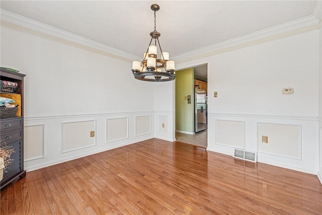 unfurnished dining area featuring a chandelier, a decorative wall, visible vents, and crown molding