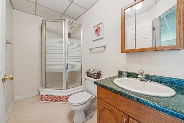 full bathroom with vanity, a drop ceiling, toilet, a stall shower, and baseboards
