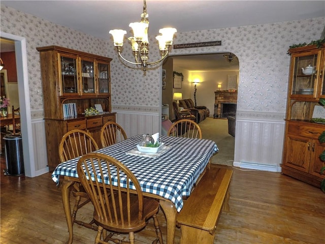 dining room with an inviting chandelier, wallpapered walls, a wainscoted wall, and wood finished floors