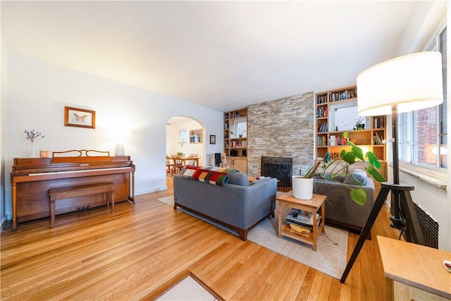 living room featuring a stone fireplace, wood finished floors, arched walkways, and built in features