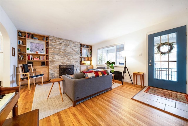 living area featuring hardwood / wood-style flooring, built in shelves, radiator heating unit, a stone fireplace, and arched walkways
