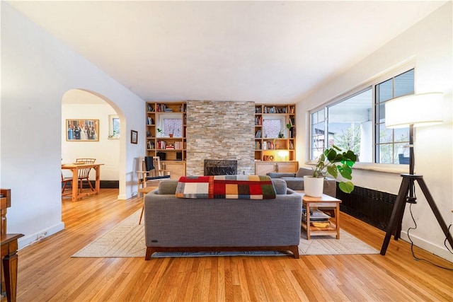 living area featuring baseboards, a fireplace, arched walkways, and light wood-style floors