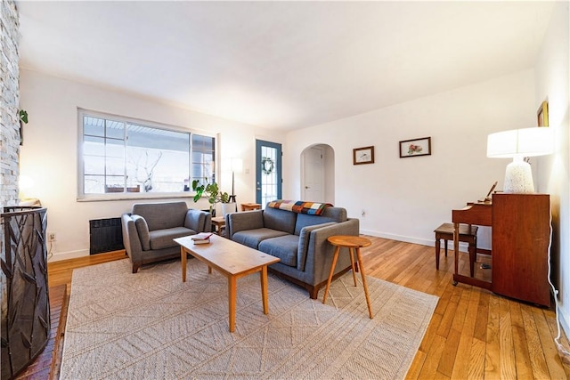 living area with radiator heating unit, arched walkways, baseboards, and light wood-style floors