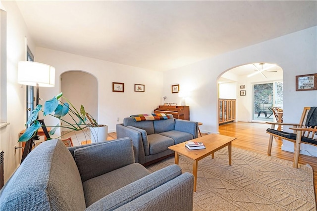 living area with arched walkways, baseboards, and light wood-type flooring