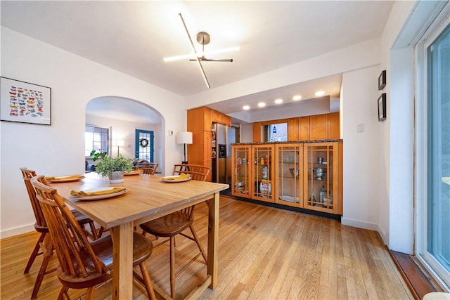 dining room featuring arched walkways, baseboards, and light wood finished floors