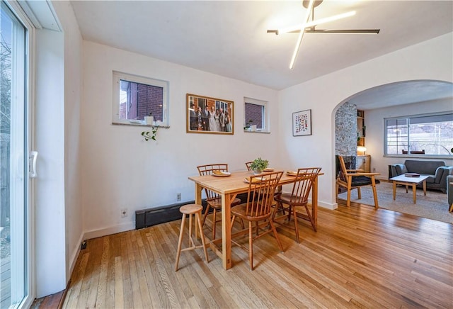 dining space with arched walkways, baseboards, and light wood-style flooring