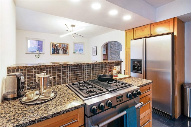 kitchen with backsplash, arched walkways, appliances with stainless steel finishes, and dark stone countertops