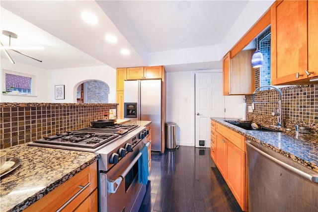 kitchen with a sink, tasteful backsplash, dark wood-style flooring, stainless steel appliances, and dark stone counters