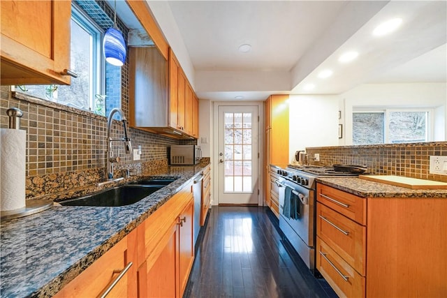 kitchen with dark stone countertops, dark wood finished floors, a sink, appliances with stainless steel finishes, and brown cabinetry