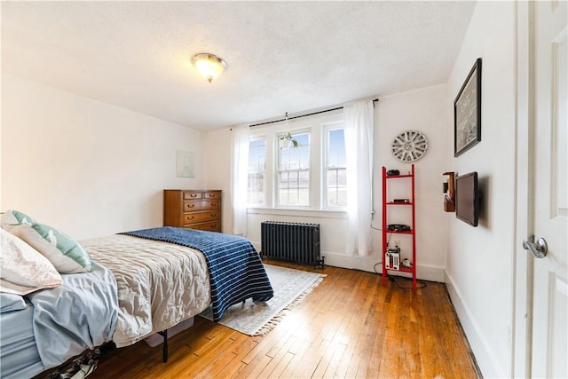 bedroom with hardwood / wood-style floors, radiator, baseboards, and a textured ceiling