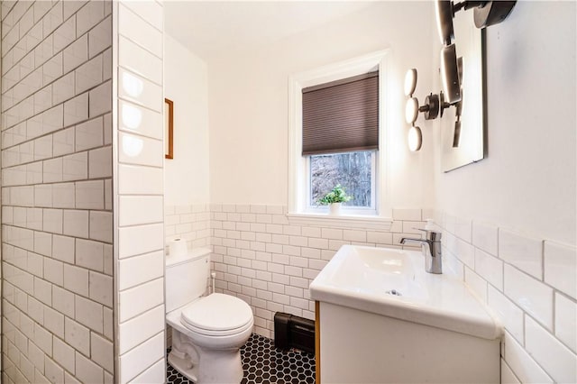 bathroom featuring toilet, vanity, wainscoting, tile patterned flooring, and tile walls