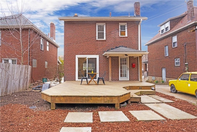 back of house with brick siding, fence, and a deck