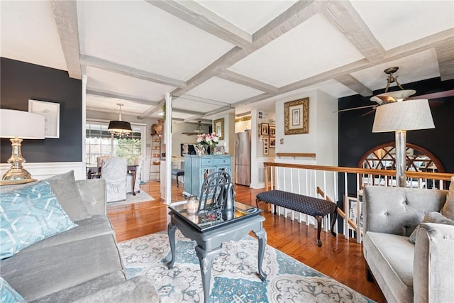 living area featuring coffered ceiling, wood finished floors, beam ceiling, and a wainscoted wall