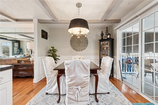 dining space with a wainscoted wall, beam ceiling, and light wood finished floors