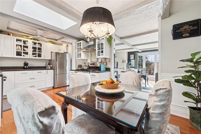 dining space with beam ceiling, coffered ceiling, a chandelier, and light wood-type flooring