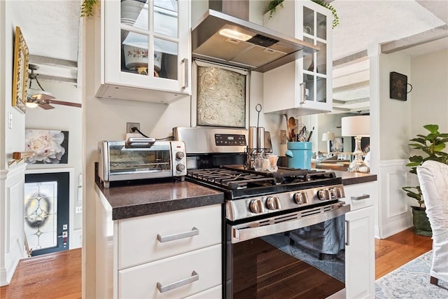 kitchen with stainless steel gas stove, range hood, white cabinetry, light wood-type flooring, and dark countertops