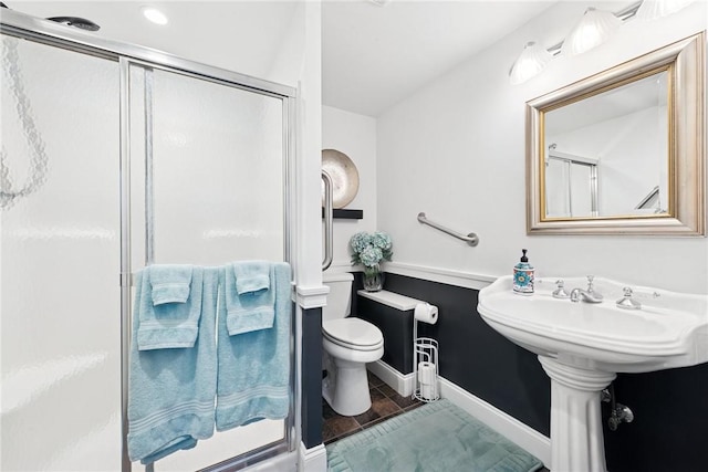 bathroom featuring toilet, baseboards, tile patterned floors, a sink, and a stall shower