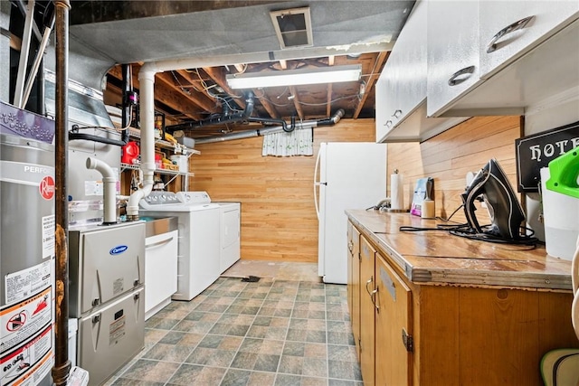 unfinished below grade area with freestanding refrigerator, wooden walls, gas water heater, visible vents, and washer and dryer