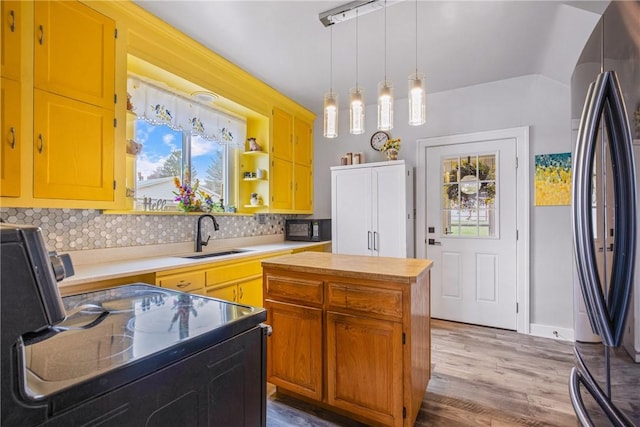 kitchen with light wood-style flooring, a sink, pendant lighting, black appliances, and backsplash