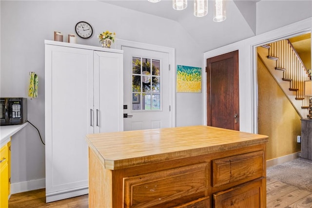 kitchen featuring light wood finished floors, baseboards, wood counters, black microwave, and vaulted ceiling