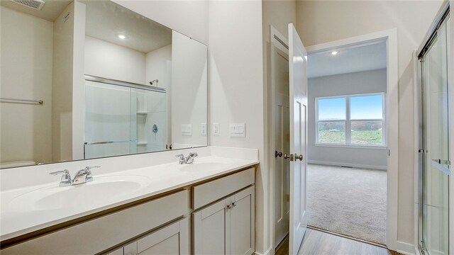full bathroom with a shower with door, double vanity, visible vents, and a sink