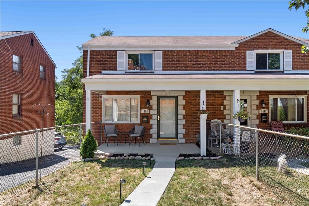 view of front of house with covered porch, brick siding, a front yard, and fence
