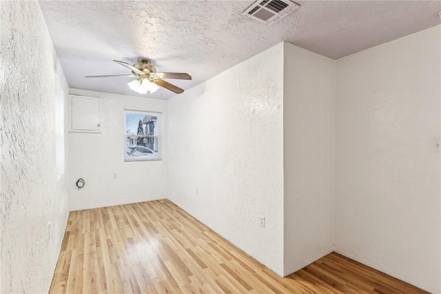spare room featuring a textured wall, visible vents, a ceiling fan, and wood finished floors