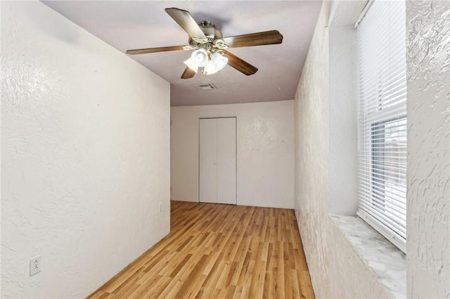 empty room with visible vents, light wood-style flooring, ceiling fan, and a textured wall