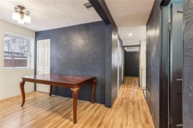 hallway with light wood finished floors, a textured wall, and visible vents