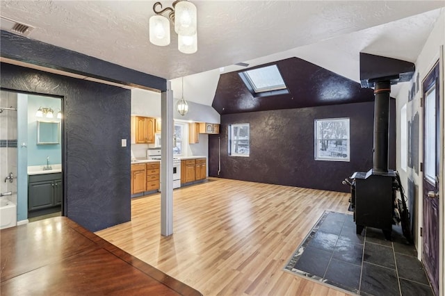 interior space featuring visible vents, an inviting chandelier, a wood stove, light wood-type flooring, and lofted ceiling with skylight