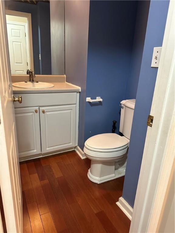 half bath with wood finished floors, toilet, vanity, and baseboards
