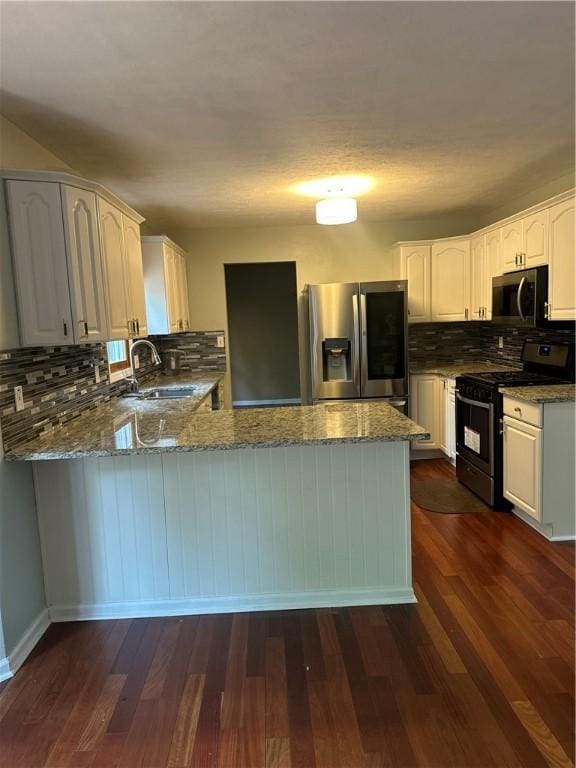 kitchen with stainless steel appliances, a sink, dark stone countertops, and a peninsula