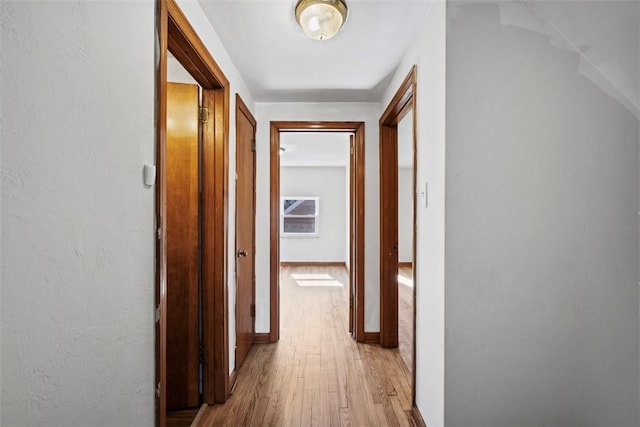 corridor with light wood-style flooring and baseboards