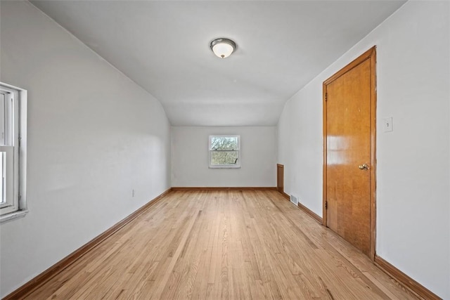 additional living space with light wood finished floors, vaulted ceiling, and baseboards