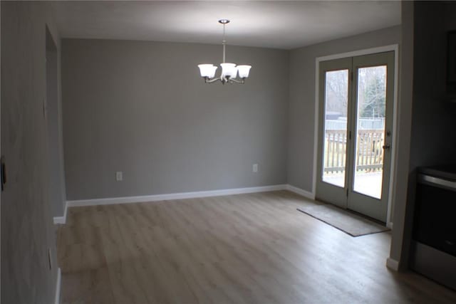 unfurnished dining area with a chandelier, wood finished floors, and baseboards