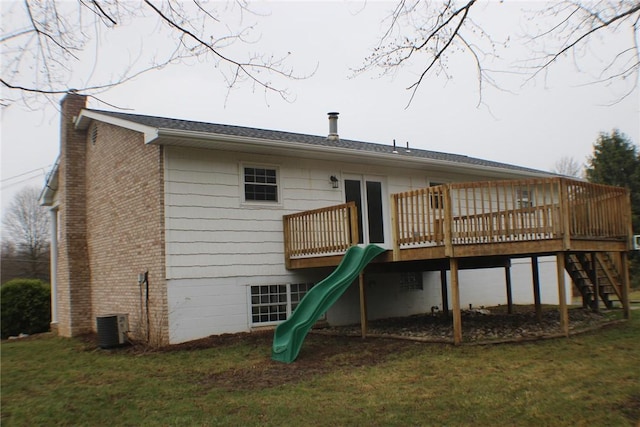 back of property featuring a chimney, a wooden deck, a playground, a lawn, and stairway