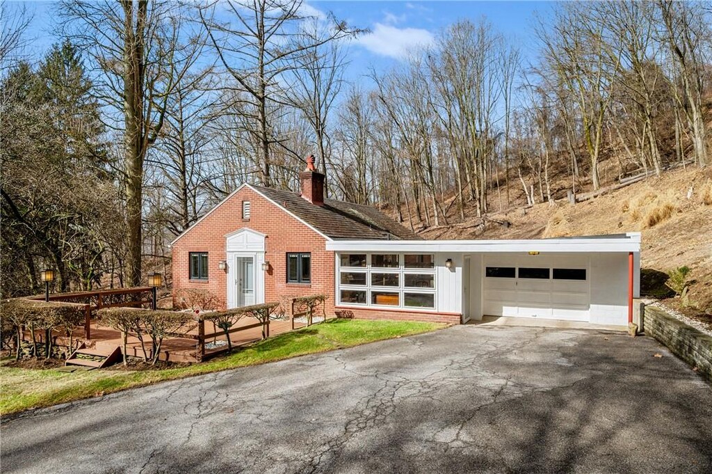 view of front facade featuring driveway, brick siding, a garage, and a chimney