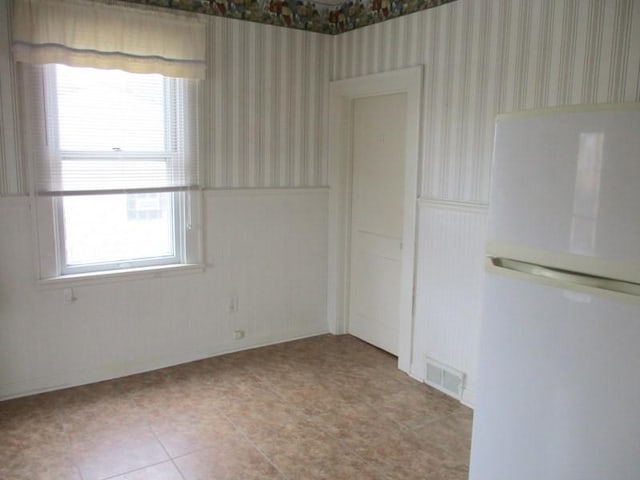 unfurnished room with wallpapered walls and a wainscoted wall