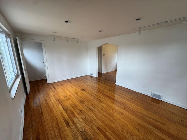 empty room with arched walkways, visible vents, wood finished floors, and baseboards
