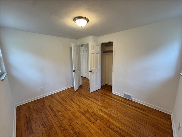 unfurnished bedroom featuring baseboards, visible vents, a closet, and wood finished floors