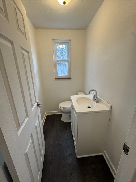 half bath with baseboards, toilet, and vanity