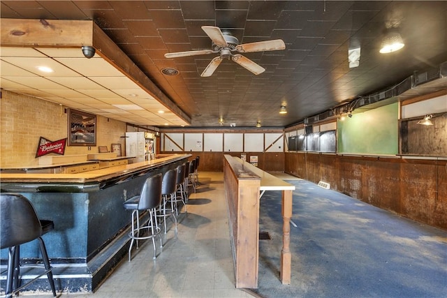 bar featuring a wainscoted wall, wood walls, a dry bar, and a ceiling fan