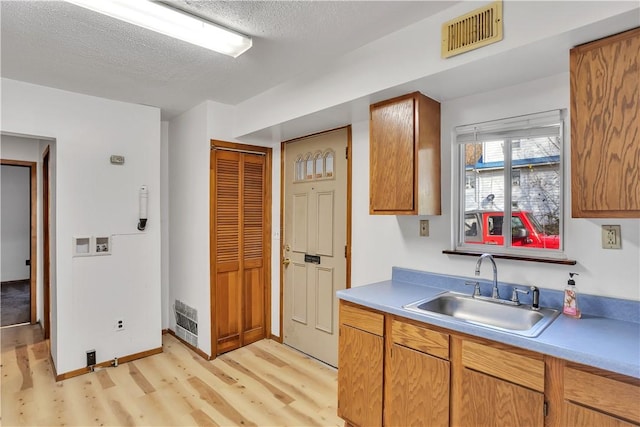 kitchen with a textured ceiling, visible vents, light countertops, a sink, and light wood-type flooring