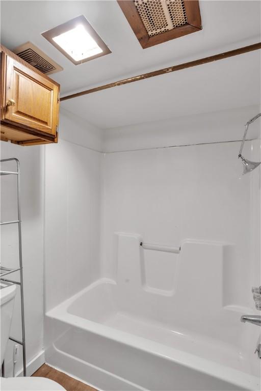 full bath with toilet, wood finished floors, shower / washtub combination, and visible vents