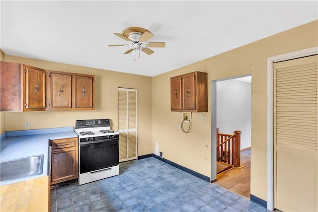 kitchen with light countertops, a sink, white gas range, baseboards, and ceiling fan