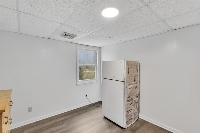 interior space featuring a paneled ceiling, visible vents, baseboards, and wood finished floors